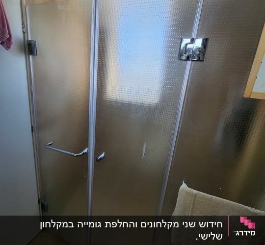 דלת מקלחת זכוכית עם ידית מתכת ומגבת תלויה